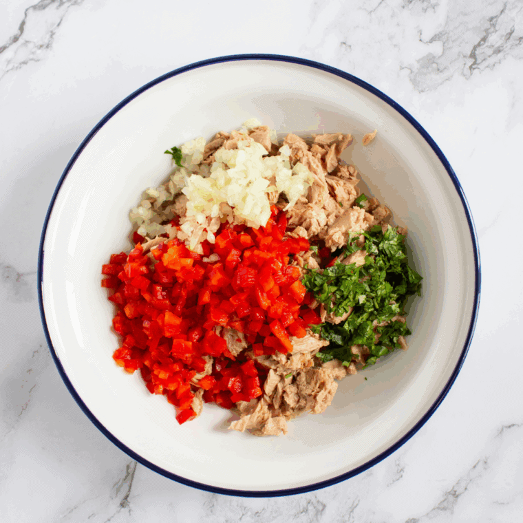 Adding chopped red bell pepper, onion, parsley, lemon juice, black pepper, and mayonnaise to the bowl.