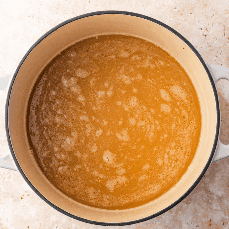 Pot of chicken broth and soy sauce simmering with sautéed garlic in sesame oil.