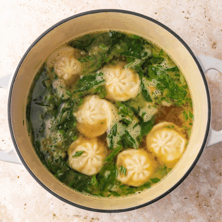 Sliced carrots, green onions, and optional spinach added to simmering dumpling soup.