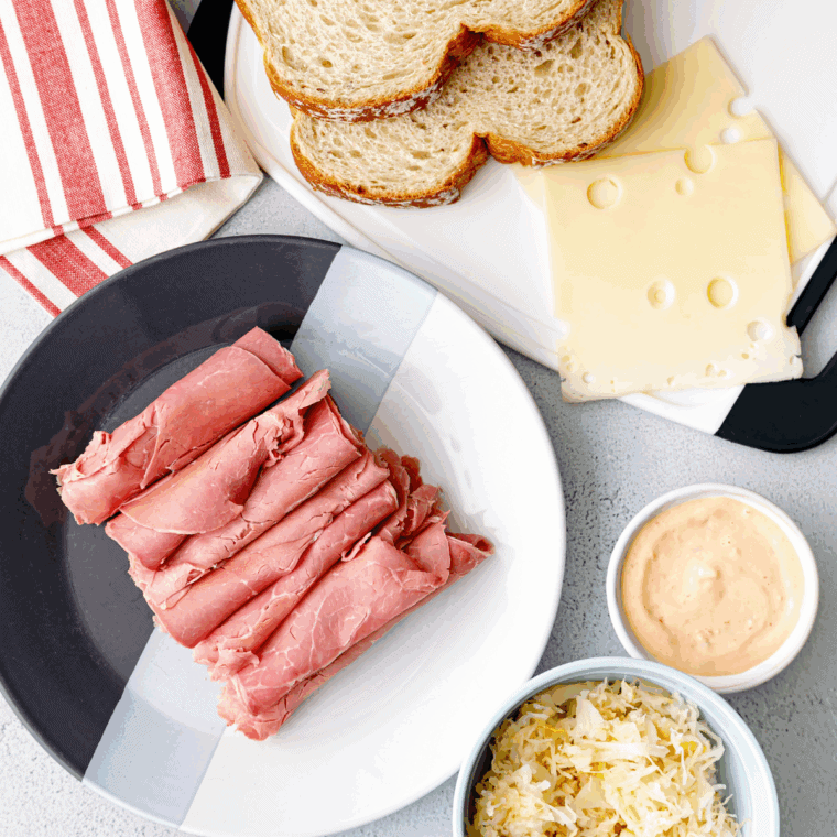 Butter being spread on slices of rye bread for a Reuben sandwich.