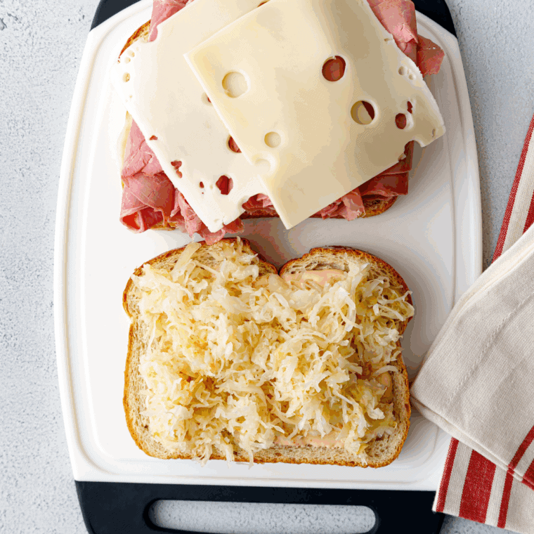 Layering corned beef, Swiss cheese, sauerkraut, and Thousand Island dressing on rye bread