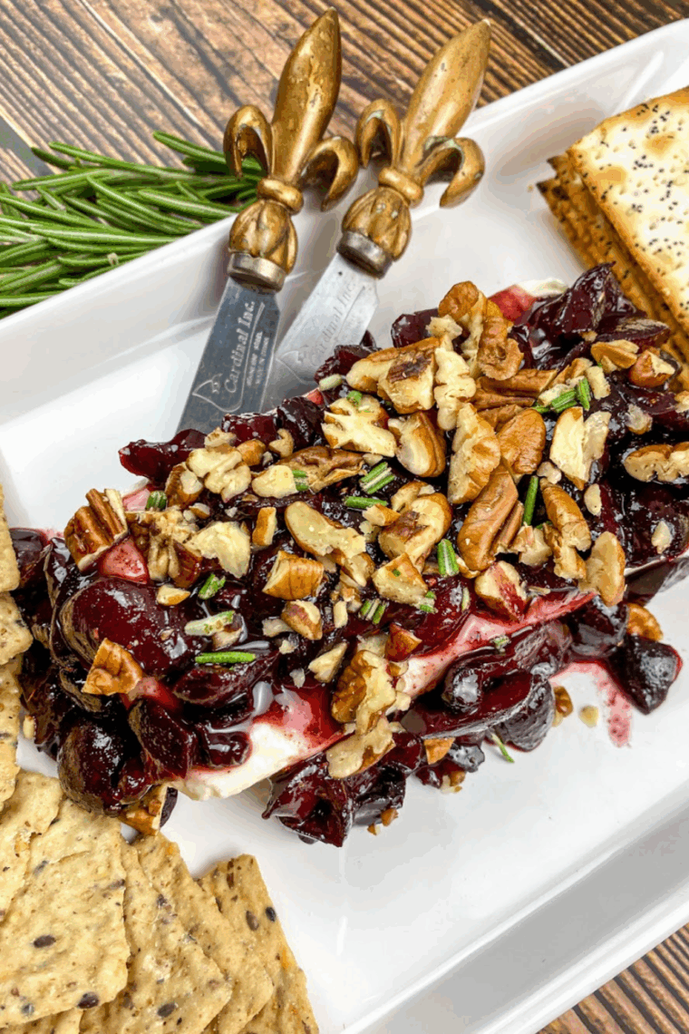 Cream cheese spread topped with warm cherry sauce, chopped pecans, and fresh herbs, served with crackers.