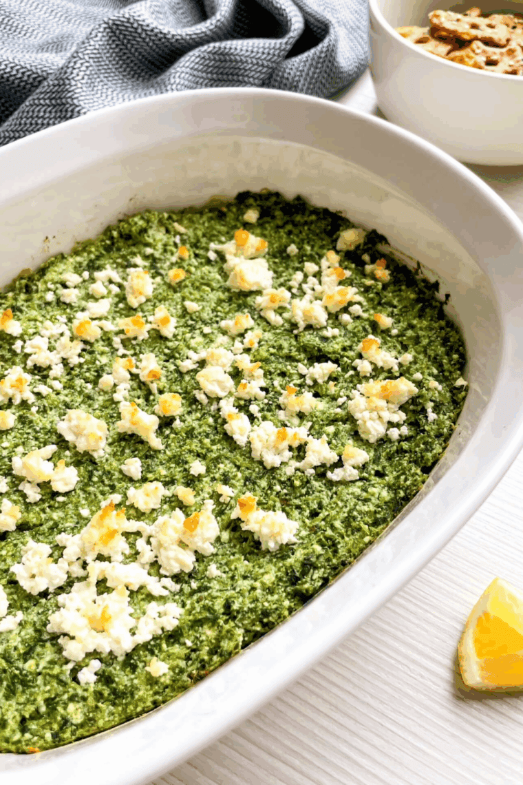 Creamy spanakopita dip in a bowl, topped with crumbled feta and fresh herbs, ready to serve.