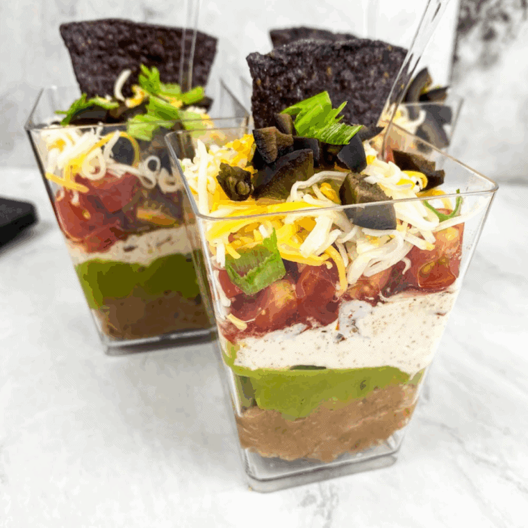 Individual 7 Layer Dip Cups with beans, cheese, guacamole, and fresh toppings.