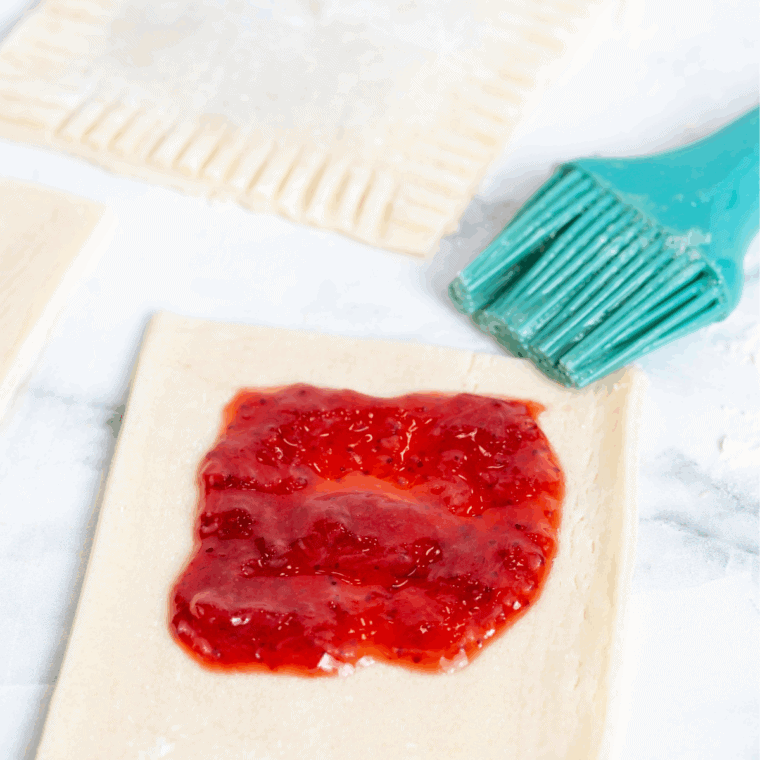 Add the Filling: Raspberry jam spooned onto the center of pie crust rectangles.