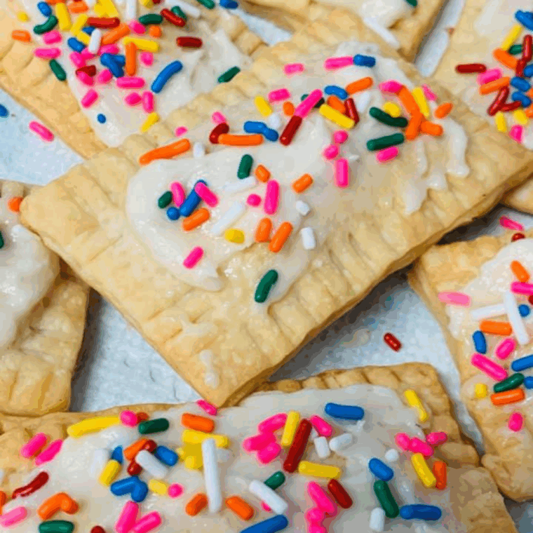 Golden air fryer raspberry pop-tarts drizzled with glaze and topped with sprinkles on a plate.