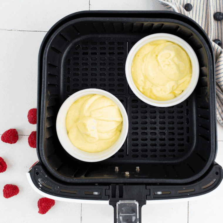 Ramekins in air fryer, puffed soufflés cooked and dusted with powdered sugar.
