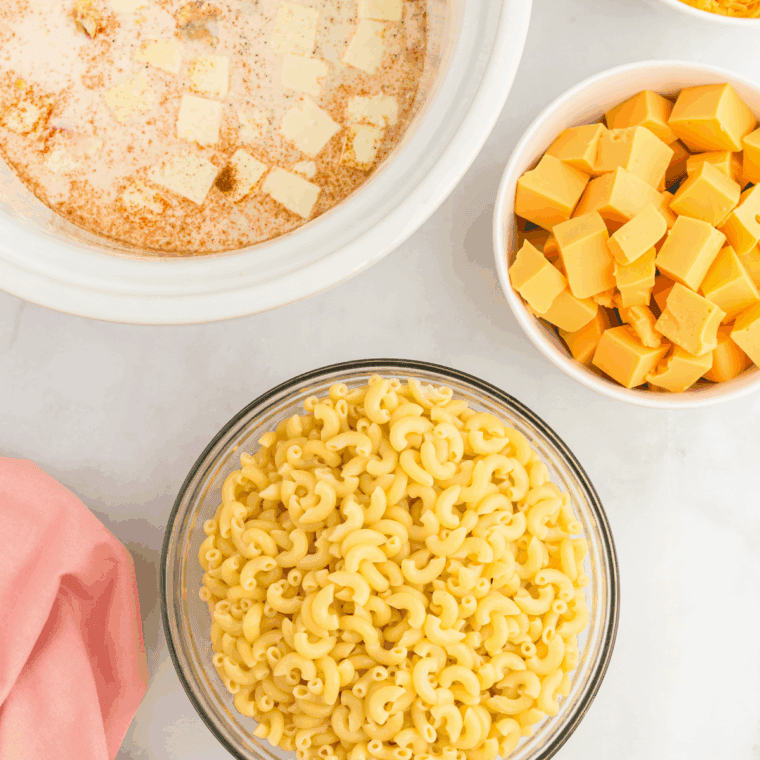Adding cooked macaroni, butter cubes, milks, and spices to crockpot for Velveeta mac and cheese