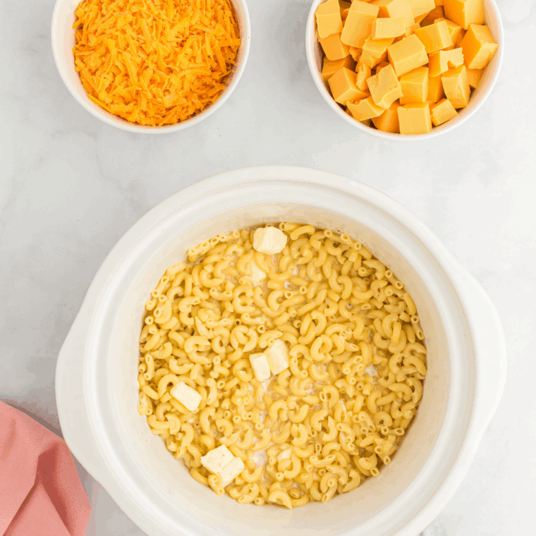 Adding cubed Velveeta and shredded sharp cheddar to crockpot mac and cheese mixture