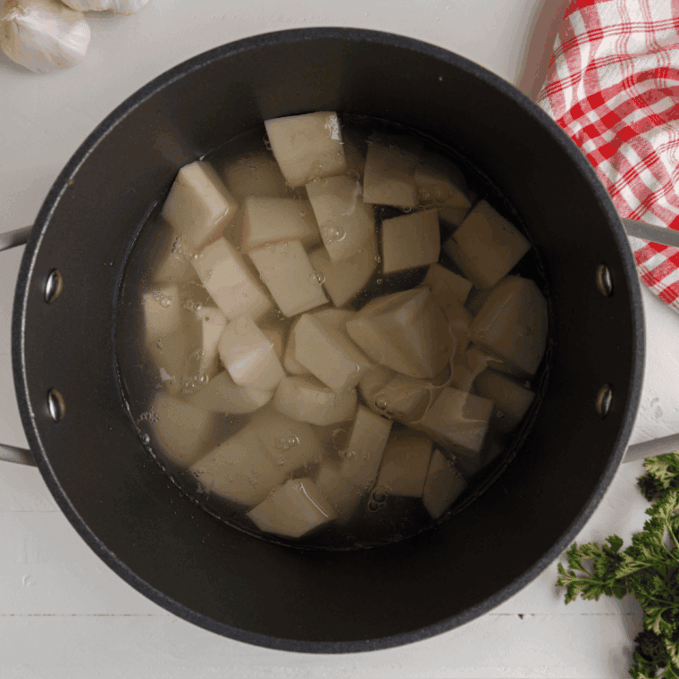 Raw Russet potatoes being boiled in a large pot of salted water.