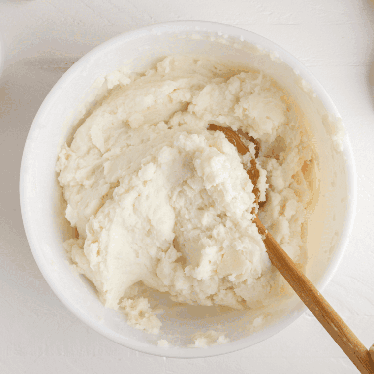 Mashed potatoes being whipped with butter and cream cheese in a pot for a fluffy texture.