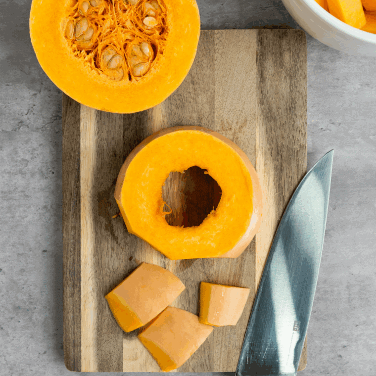Chopped butternut squash, diced carrots, onions, apple, and minced garlic on a wooden cutting board ready for soup preparation.