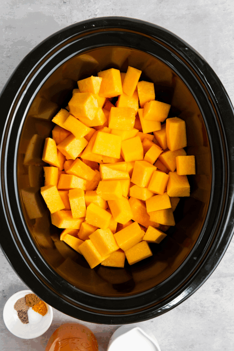 Slow cooker filled with butternut squash soup ingredients cooking on low heat.