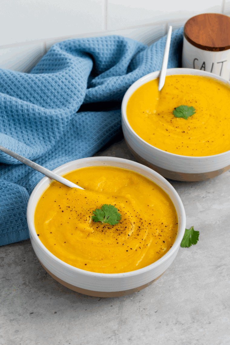 A warm bowl of creamy Ina Garten butternut squash soup served with a drizzle of cream and fresh thyme on top.