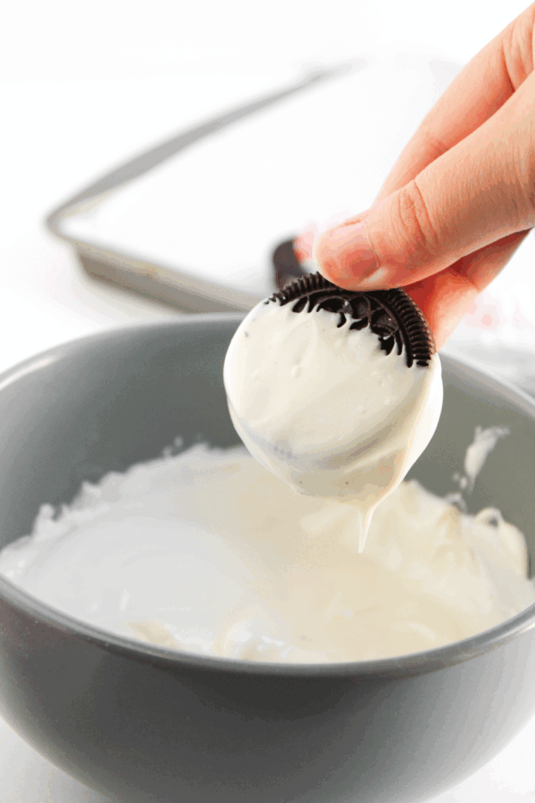 A bowl of white chocolate wafers being melted in a microwave, illustrating the process of heating in 30-second intervals and stirring until smooth.
