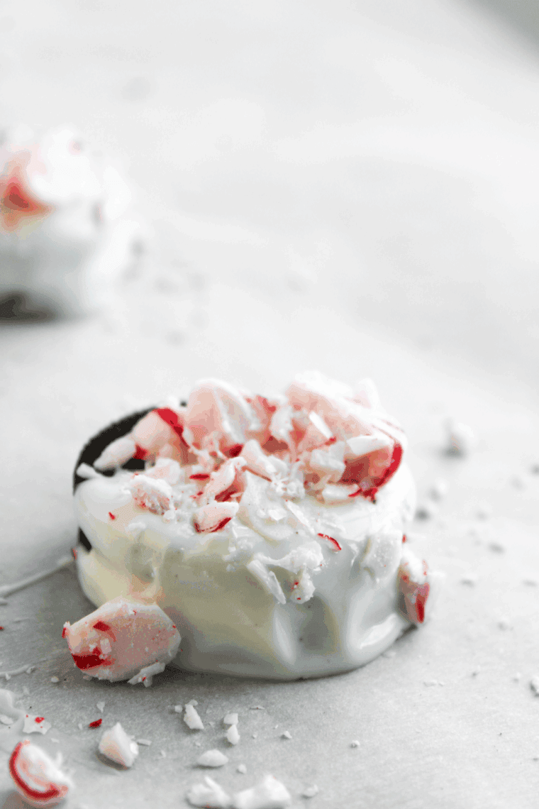 Stack of finished Peppermint White Chocolate Covered Oreos, dipped in white chocolate and topped with bright red crushed peppermint candies.