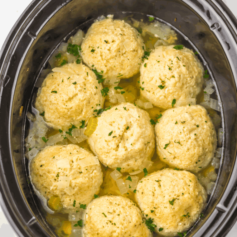 Shredded cooked chicken being returned to the slow cooker next to floating matzo balls simmering in the golden broth.