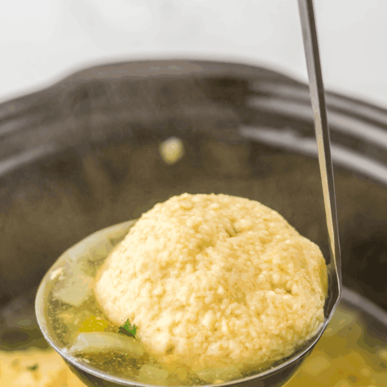 Chicken, carrots, celery, and herbs simmering inside a slow cooker pot for matzo ball soup.