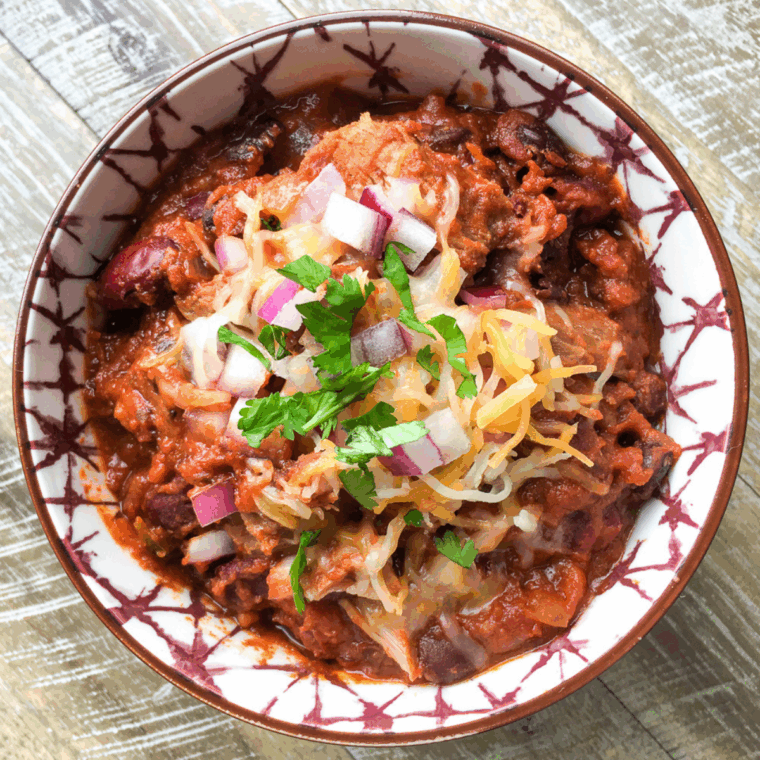Bowl of hearty Slow Cooker Pulled Pork Chili topped with cheese and fresh herbs.