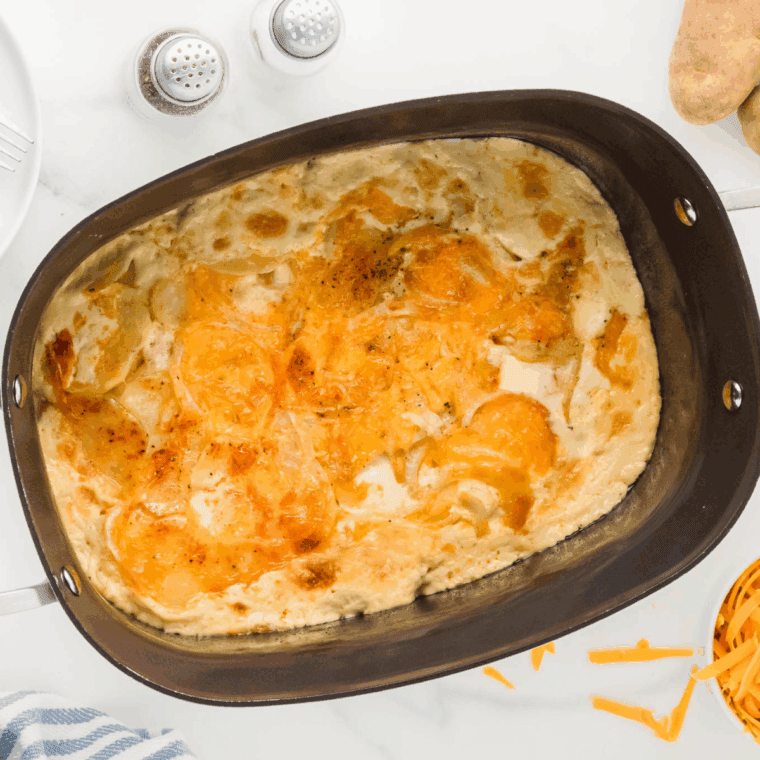 Creamy, cheesy scalloped potatoes baked until golden, visible in a slow cooker insert or transferred to a serving dish.