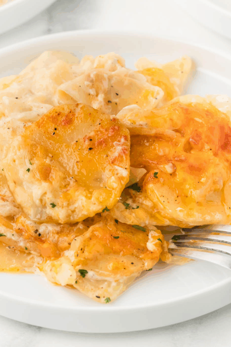 Creamy, cheesy scalloped potatoes baked until golden, visible in a slow cooker insert or transferred to a serving dish.