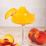 Frozen peach bellini slushi served in a glass with a straw, made using a Ninja Slushi.