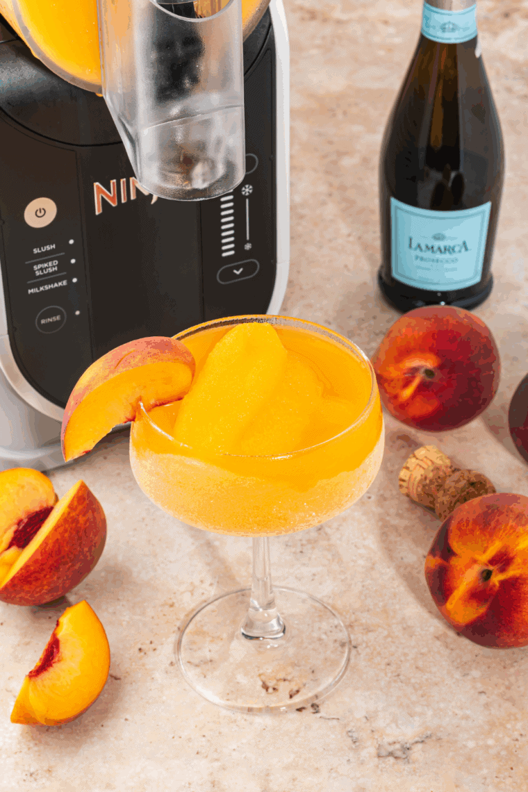 Frozen Peach Bellini slushi served in a glass with straw, made using a Ninja Slushi.