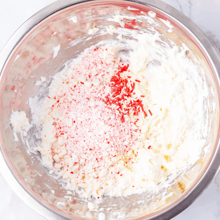 Peppermint fluff in a serving bowl topped with red and white sprinkles, served with chocolate wafer cookies.