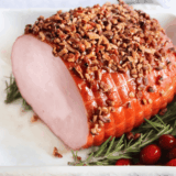 Golden-brown air fryer Christmas ham sliced and served on a platter with herbs.
