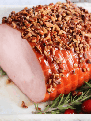 Golden-brown air fryer Christmas ham sliced and served on a platter with herbs.