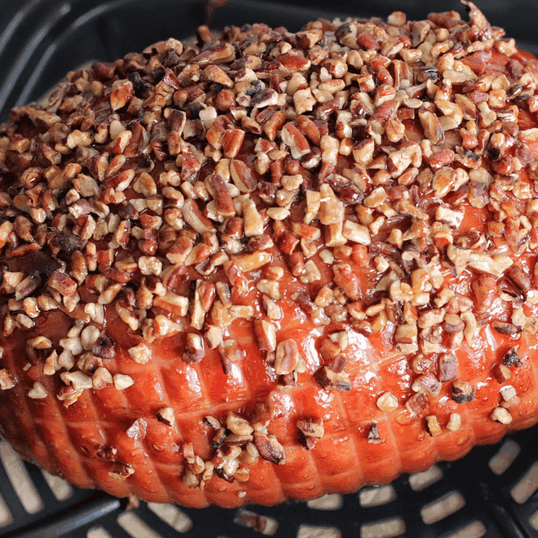 Golden-brown air fryer Christmas ham sliced and garnished with fresh herbs on a festive platter.