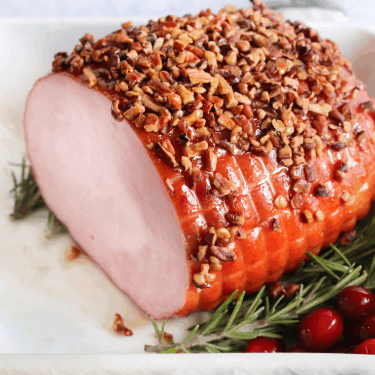 Golden-brown air fryer Christmas ham sliced and served on a platter with herbs.