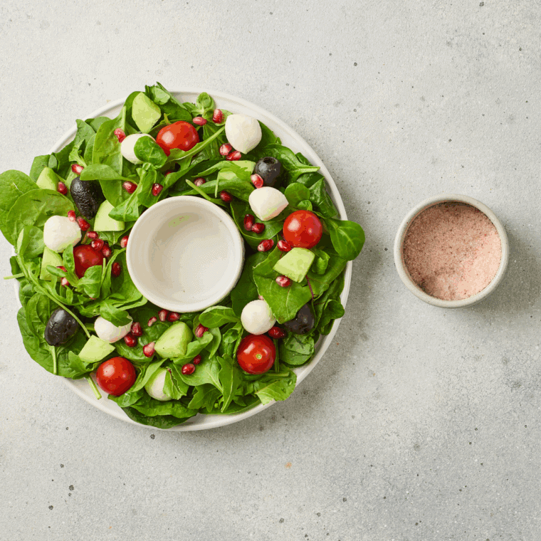 Cherry tomatoes, mozzarella balls, black olives, pomegranate seeds, and fresh basil evenly scattered over greens for a festive wreath salad.