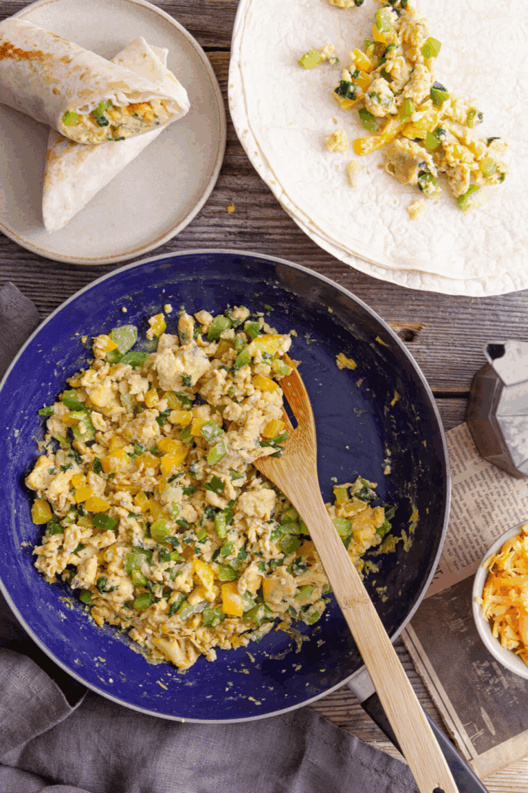 Whisked eggs cooking with sautéed vegetables in a skillet.