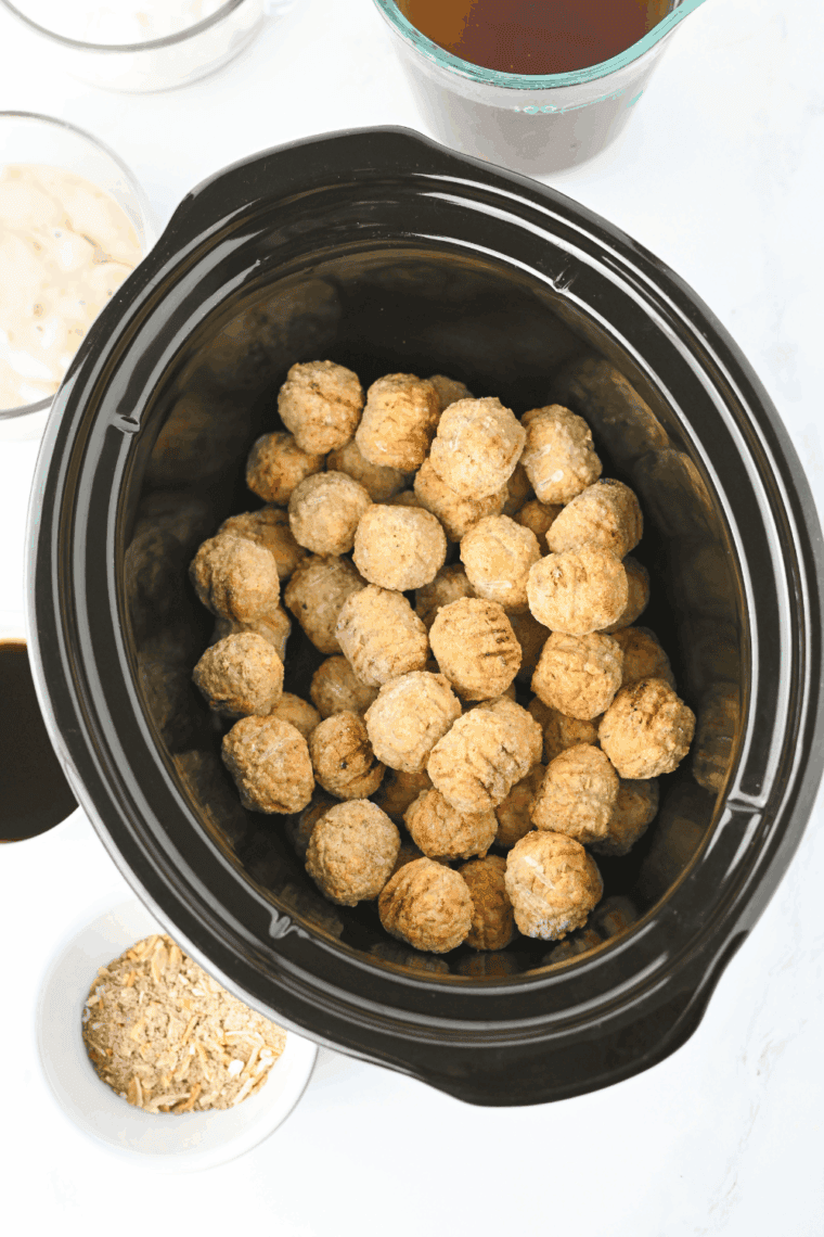 Placing pre-cooked meatballs into a crockpot for cooking.