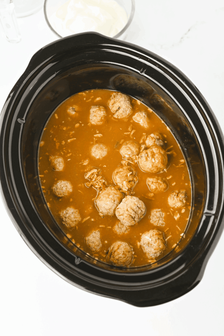 Stirring sour cream into crockpot meatballs for creamy sauce.