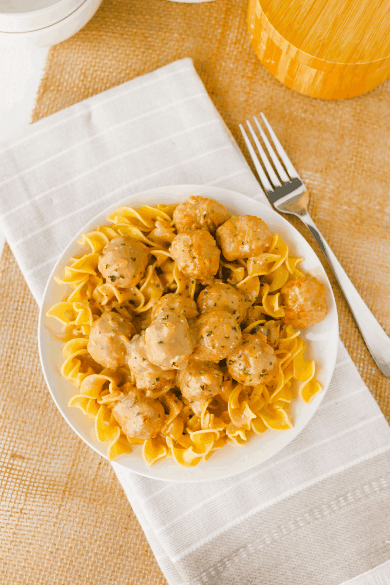 Serving Swedish meatballs and sauce over egg noodles on a plate.
