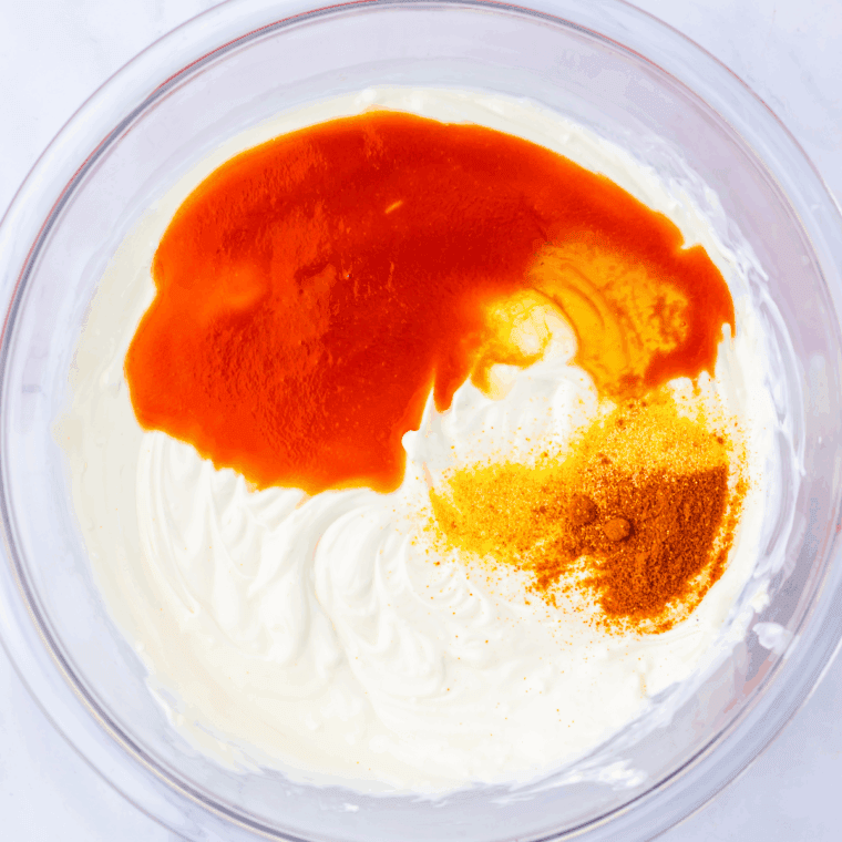 Mixing softened cream cheese and buttermilk in a microwave-safe bowl for Nashville Hot Chicken Dip.