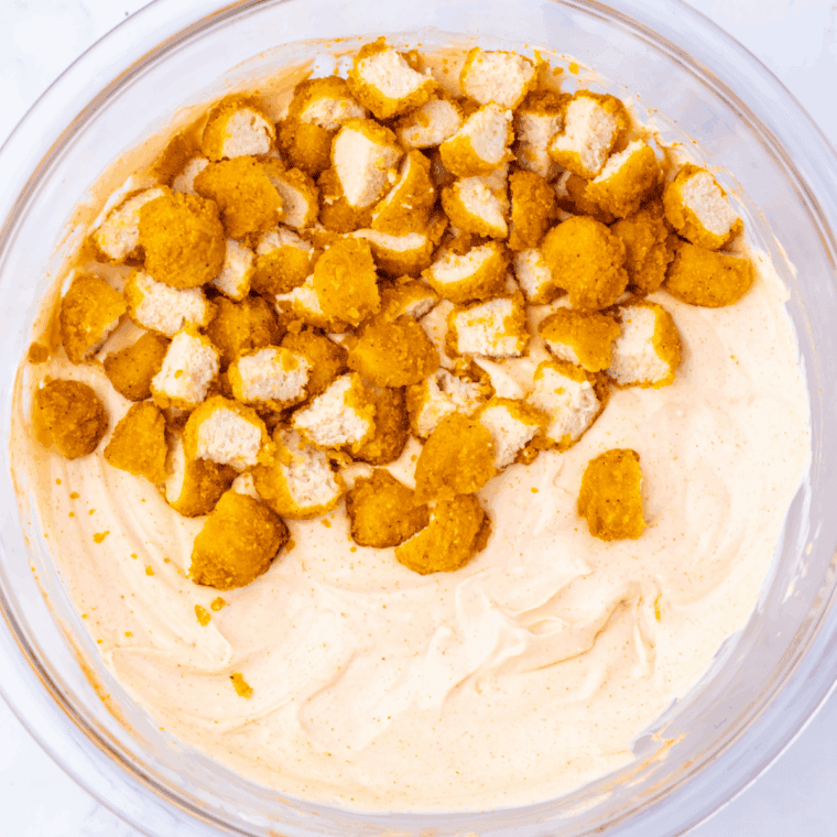 Stirring spices, hot sauce, and chopped popcorn chicken into the creamy dip mixture.