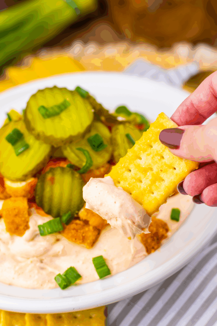 Easy Nashville Hot Chicken Dip served in a bowl with popcorn chicken, pickles, scallions, and spicy sauce.