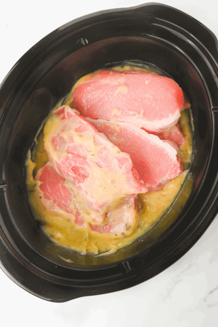 Boneless pork chops added to the creamy ranch sauce in the crockpot, coated evenly.