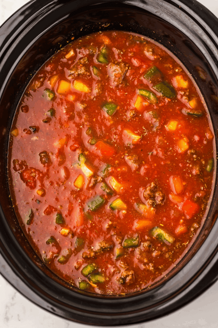 Close up of Stuffed Pepper Soup simmering in a slow cooker with visible chunks of green bell pepper and ground beef.