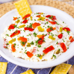 Easy Texas Christmas Dip in a bowl topped with chiles, cheese, and festive garnishes surrounded by tortilla chips.