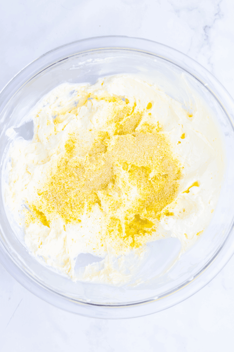 Mixing cream cheese and mayonnaise in a bowl with hand mixer, adding onion powder and garlic salt.