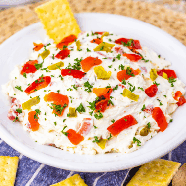 Easy Texas Christmas Dip in a bowl topped with chiles, cheese, and festive garnishes surrounded by tortilla chips.