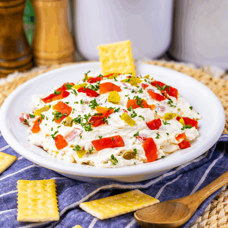 Easy Texas Christmas Dip in a bowl with melted cheese, roasted red peppers, and jalapeños, served with crackers and vegetables.