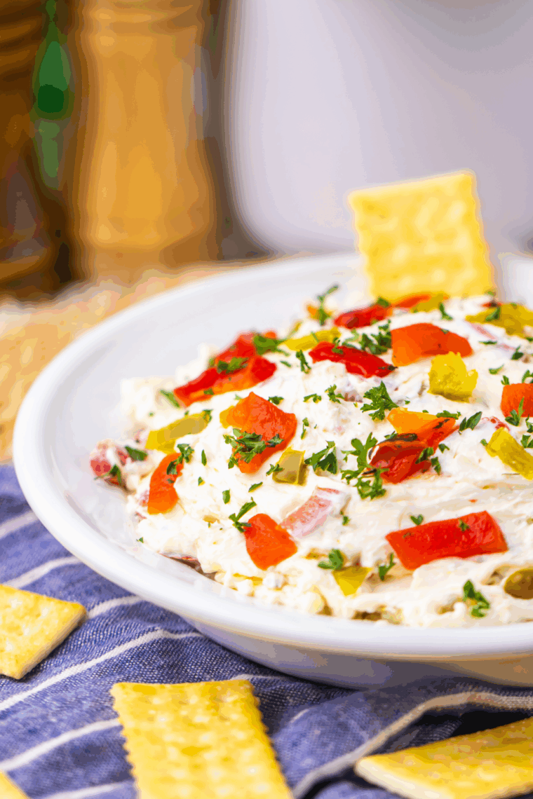 Easy Texas Christmas Dip in a bowl topped with melted cheese, roasted red peppers, and jalapeños, served with tortilla chips and fresh vegetables.