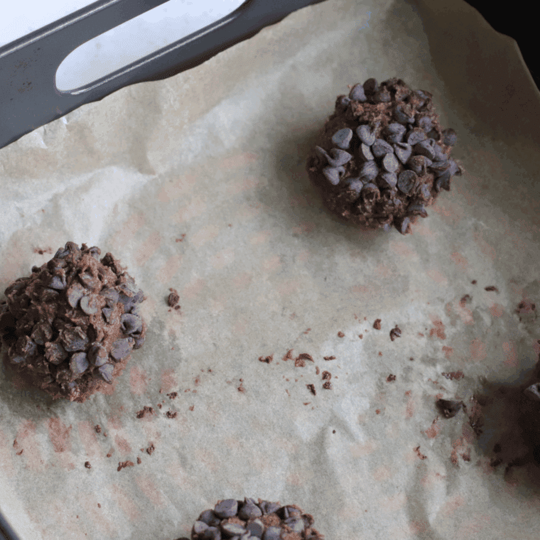 Cookie dough portioned into small balls, rolled in chocolate chips, and spaced on parchment paper in the air fryer basket.
