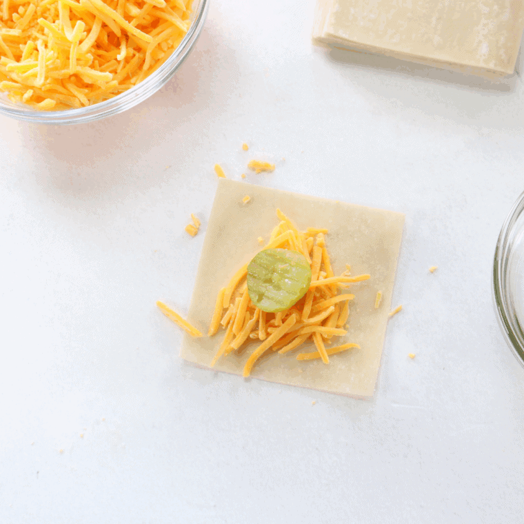 Pickle slice and cheese placed on wonton wrapper, ready to fold