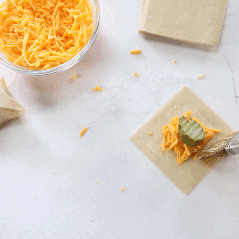 Pickle slice and cheese placed on wonton wrapper, ready to fold